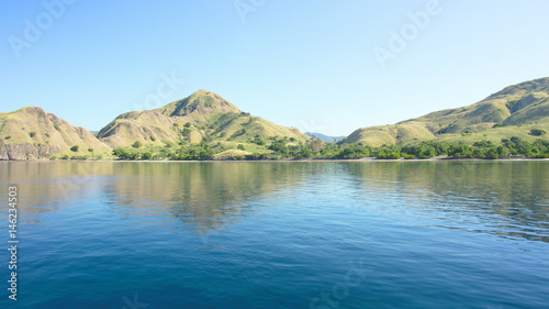 Coastline of mountains with green vegetation reflected  in blue ocean water at Labuan Bajo in Flores  Indonesia.