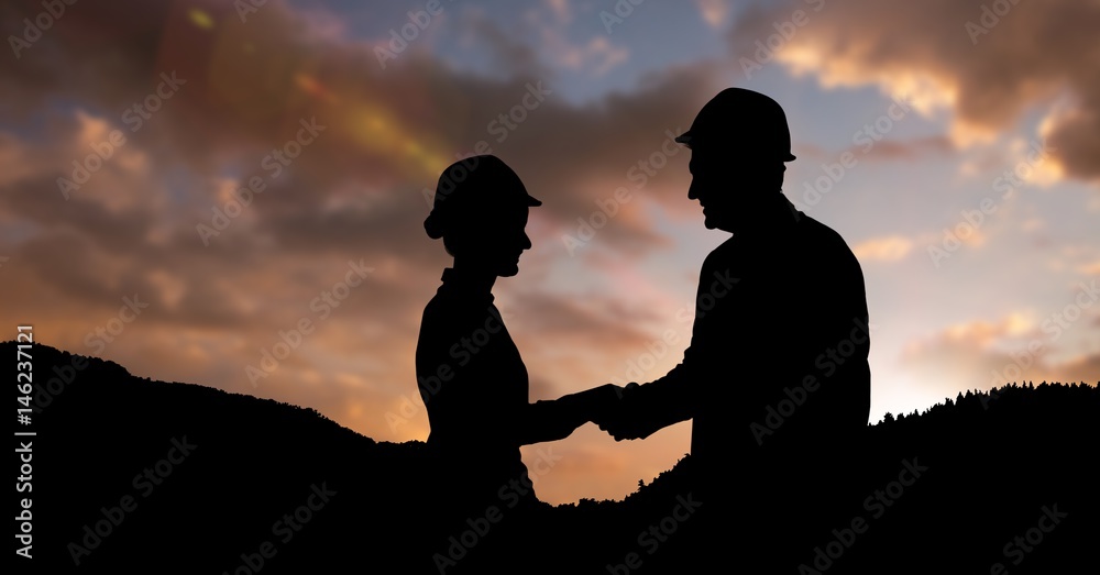 Silhouette professionals wearing hardhats while shaking hands