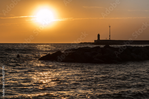 Silhouette of Lighthouse, Reef, and Choppy Sea at Sunset