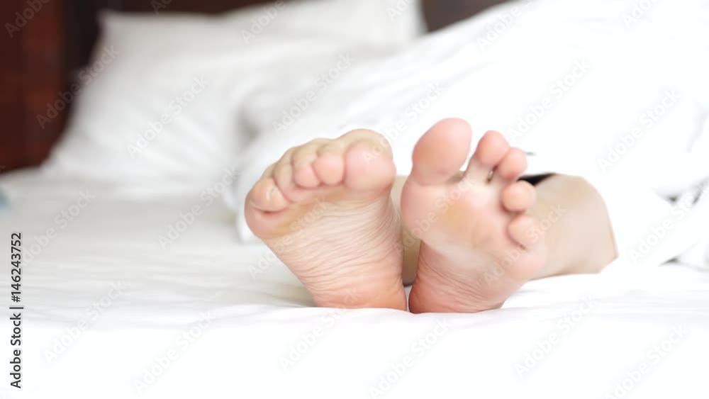 Delicate female feet moving toes playfully on white bedding Delicate female feet moving toes playfully on white bedding