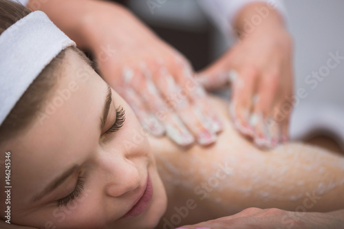 Young smiling woman getting firming sugar scrub therapy on her back