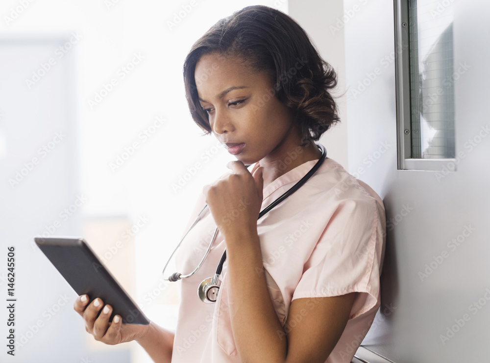 Mixed Race nurse using digital tablet leaning on door Mixed Race nurse using digital tablet leaning on door