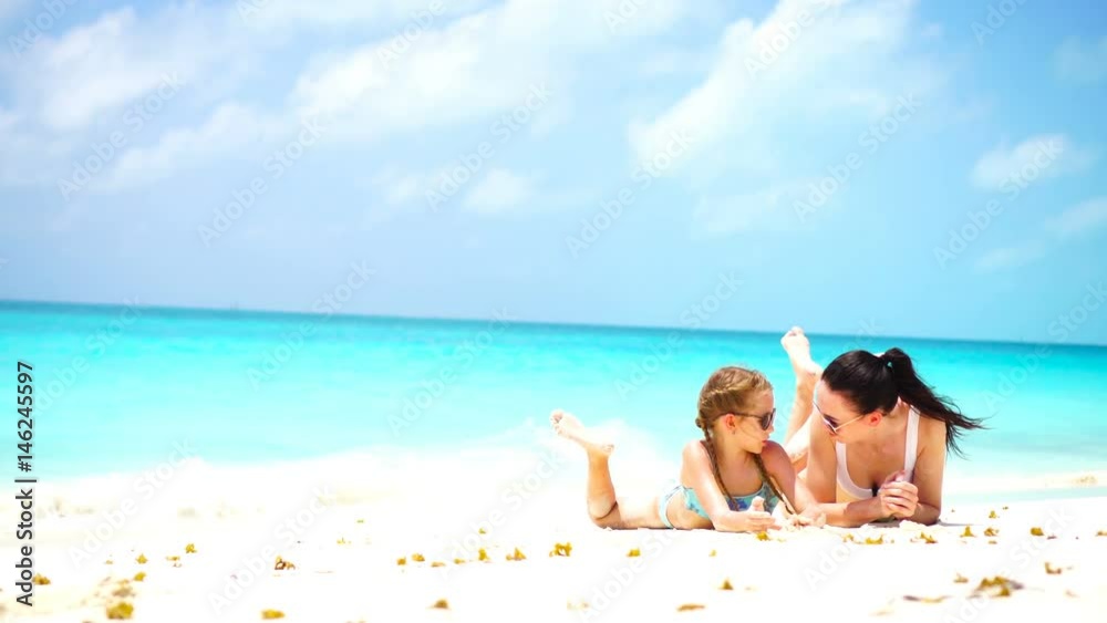 Little adorable girl and young mother at tropical beach lying on white beach and enjoy their summer vacation Little adorable girl and young mother at tropical beach lying on white beach and enjoy their summer vacation