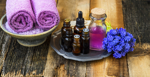 Spa setting.Oil bottles with purple flowers and soft towels on wooden rustic background