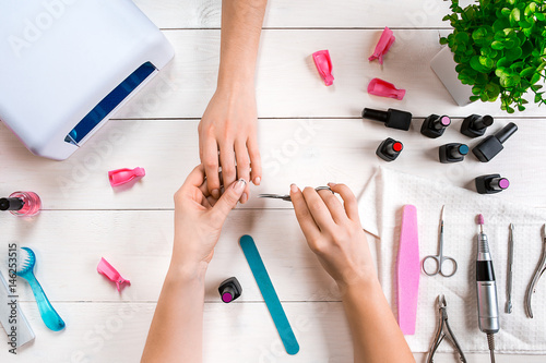 Nail care. Closeup of female hands filing nails with professional nail file in beauty nail salon. Top view