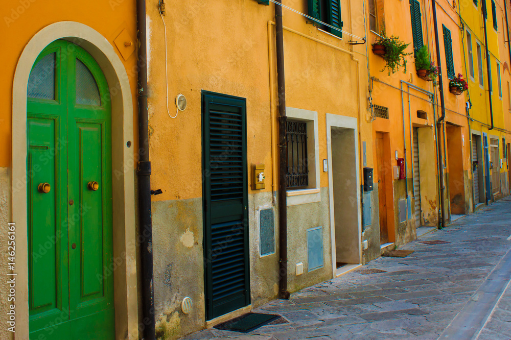 Bright narrow street with yellow houses in traditional Italian style. Green door on the frontview