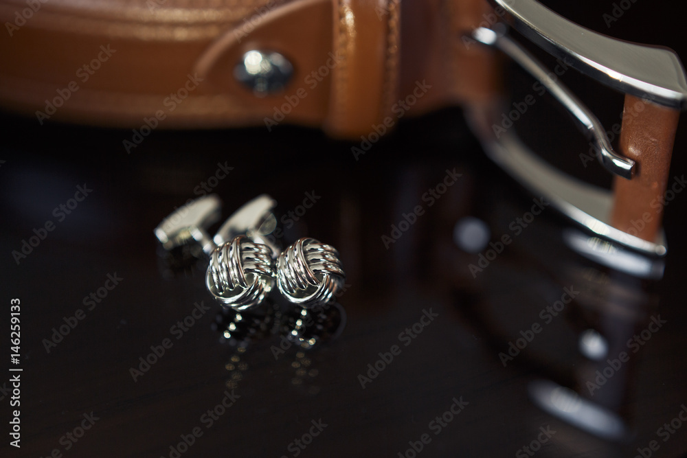 Silver cufflinks lie before the leather belt Silver cufflinks lie before the leather belt