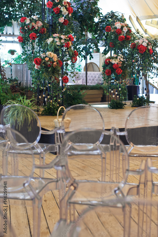 White chairs with transparent bacns stand before stage with flowers