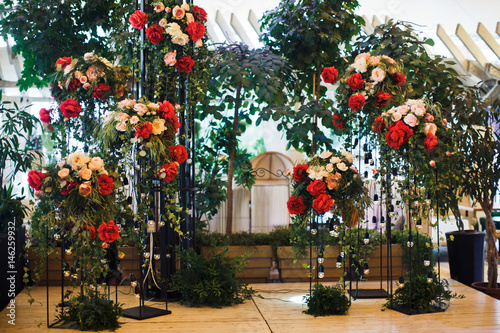 Bouquets of large red flowers and roses stand on tall steel pillars in the room