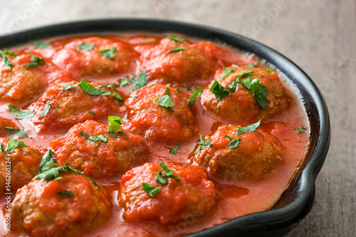 Meatballs with tomato sauce in iron frying pan on wooden table