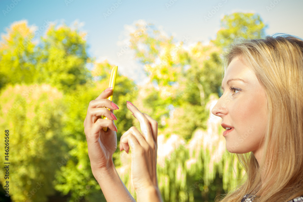 Woman sitting in park, using phone taking pictures Woman sitting in park, using phone taking pictures
