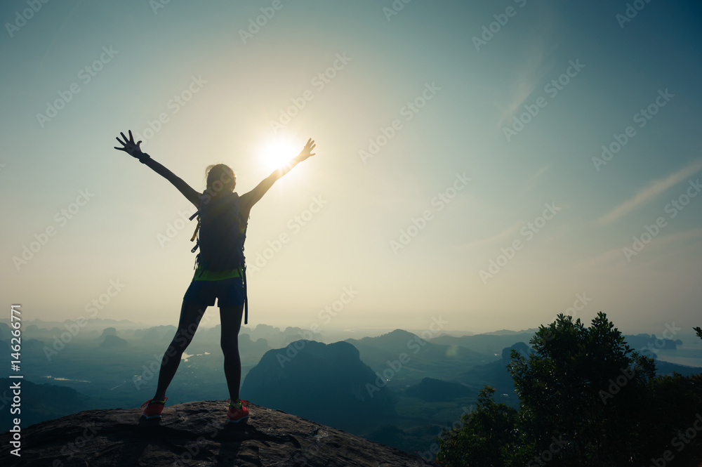cheering successful woman hiker open arms on sunrise mountain top