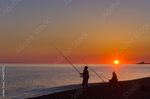 Beautiful scene with fisherman silhouette with rod sitting on sea beach