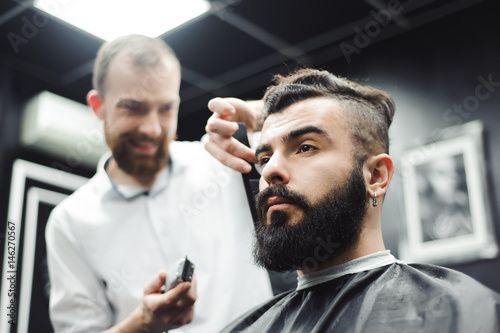 Master cuts hair and beard of men in the barbershop, hairdresser makes hairstyle for a young man