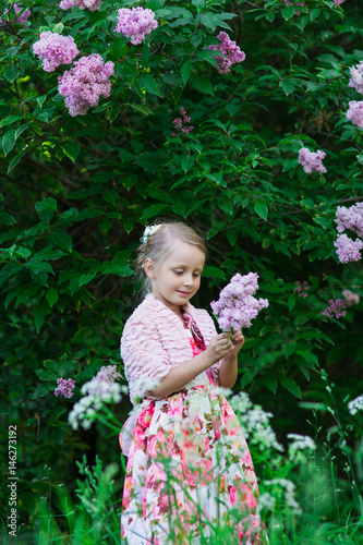 Beautiful cute girl with bouquet of lilacs in park on summer day against the background of blossoming tree