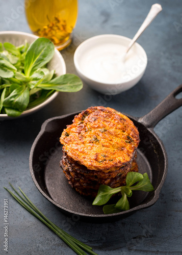 Sweet potato fritters in skillet served with fresh green salad, yogurt sauce and olive oil