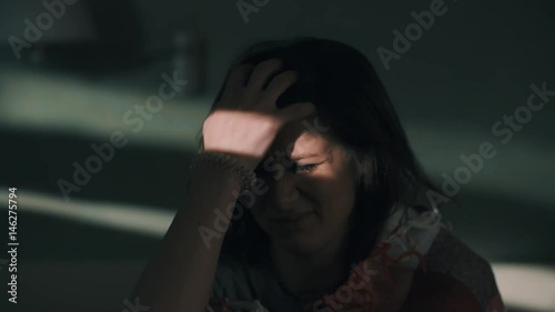 Young pretty drowsy caucasian brunette girl wakes up and sits on bed. Beam of light falls on her face in early morning, close up slow motion, cold tone