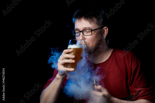 The man at the same time drinks beer and smokes an electronic cigarette.