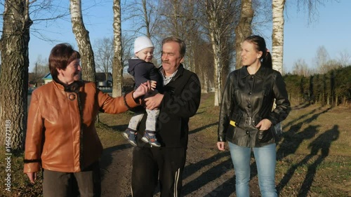 A large family walks in the park near the road at sunset. Grandmother and grandfather are talk with their grandson and daughter
