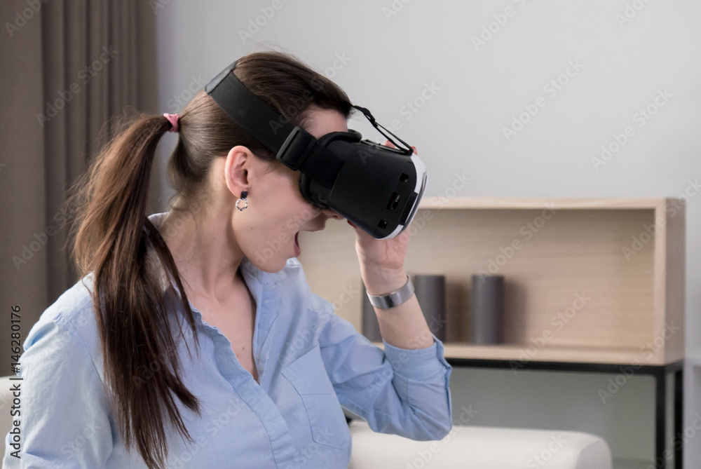 Excited Caucasian female in casual clothes using VR headset indoors, watching 360 video at home Excited Caucasian female in casual clothes using VR headset indoors, watching 360 video at home
