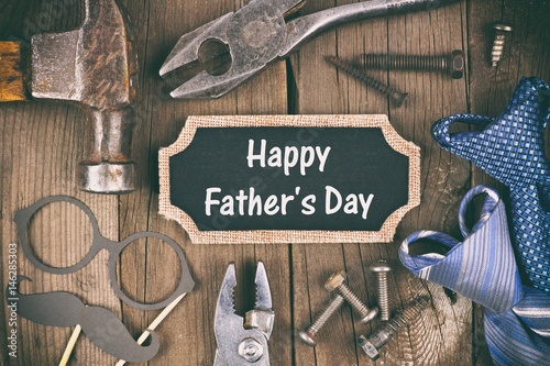 Happy Fathers Day message on a chalkboard tag with frame of tools and ties on a wooden background, vintage styling