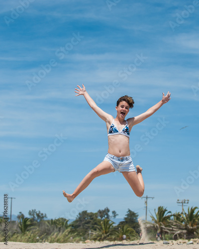 Teenage girl jumping for joy with the blue California Spring sky in background.