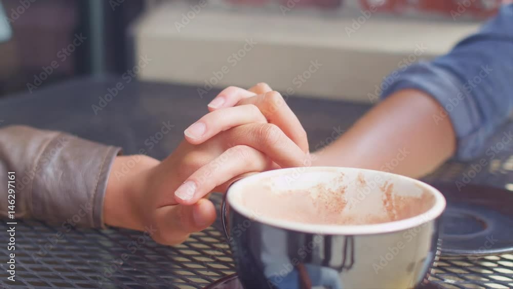 Close up of a couple holding hands across the table on a coffee date