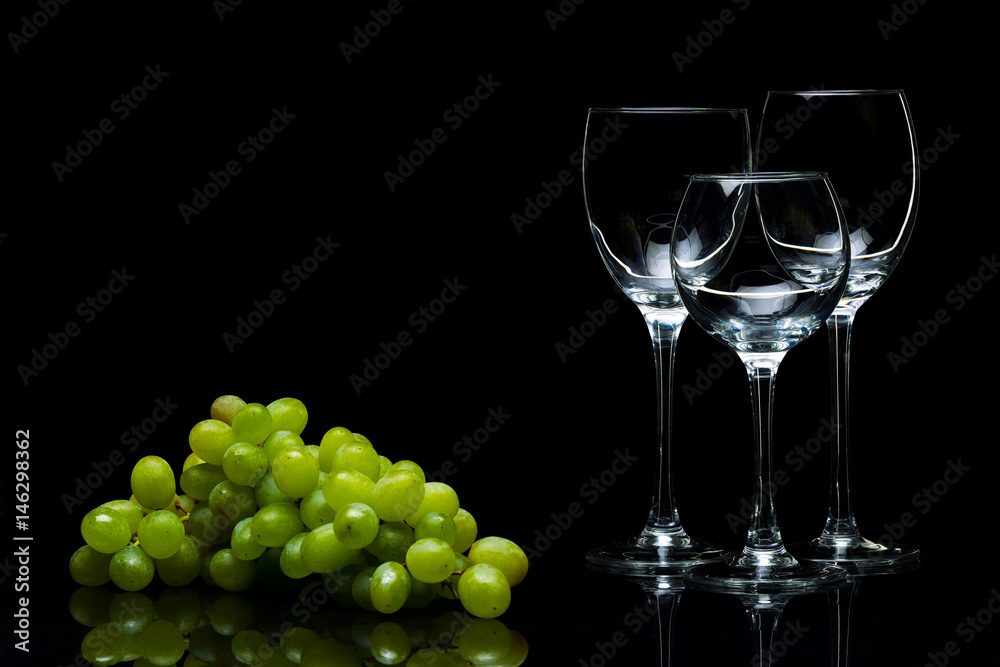 Glasses for wine and a bunch of grapes on a black background