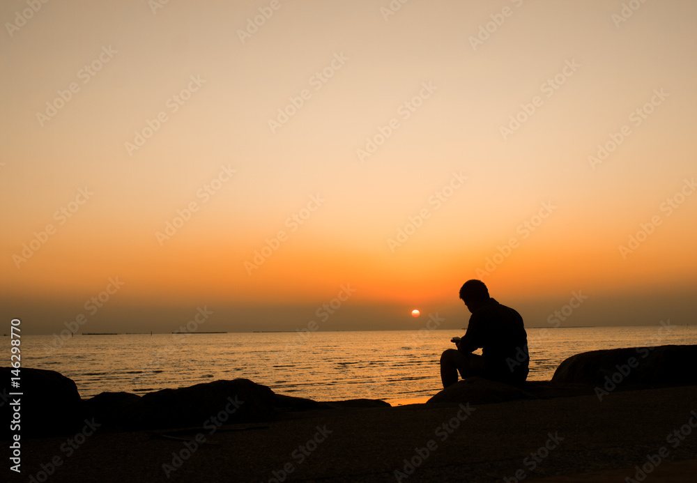 Silhouette of young man, standing alone, lonly by the sunset light of sea