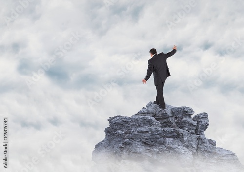 Business man walking up mountain peak in the clouds