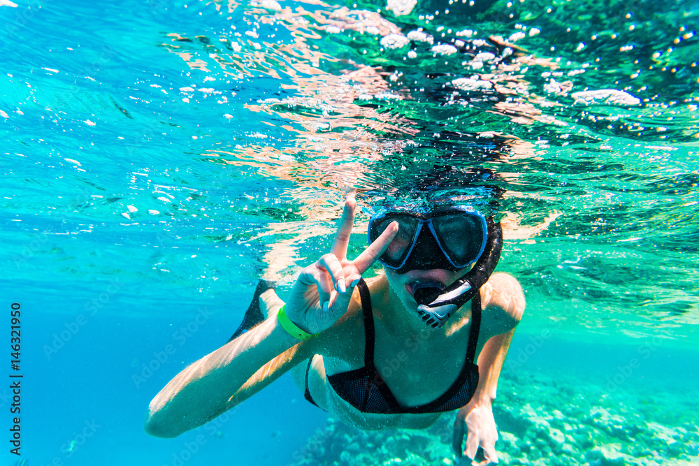 Woman underwater snorkeling with victory sign swimming in sea