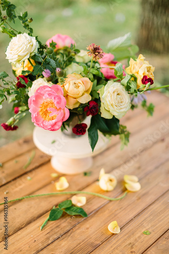 bouquet, flower, gifts and floral arrangement concept - top view on fresh bouquet of yellow and white roses, red carnations, pink charming peon, shoots of wild rose, in white vase on wooden table