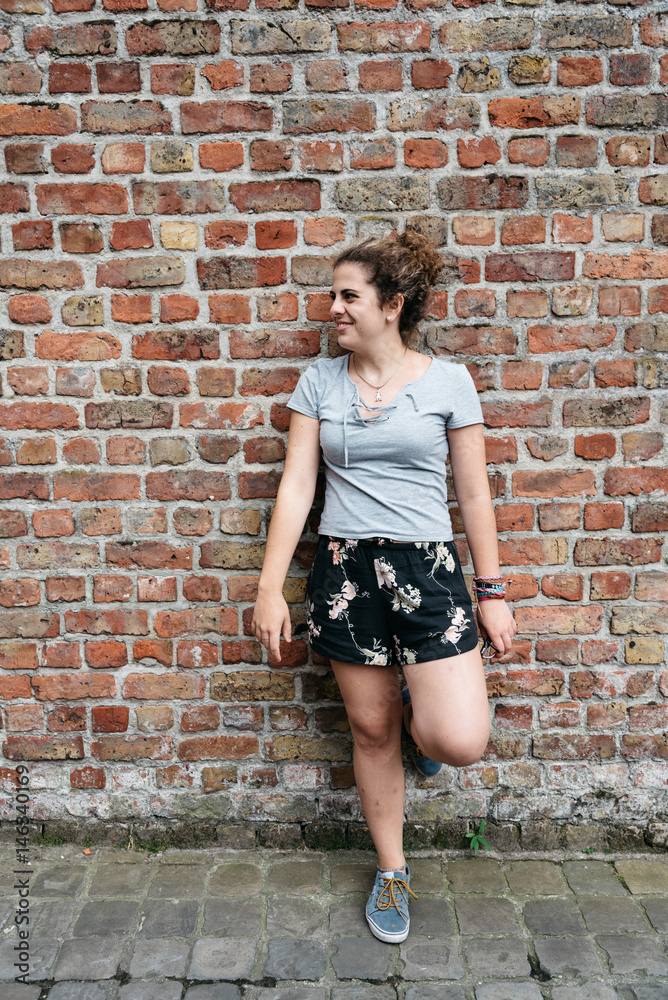 Full length portrait of smiling expression young adult woman leaning against brick wall. Full length portrait of smiling expression young adult woman leaning against brick wall.