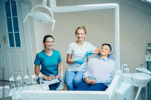Female dentist  herassistent and happy smiling patient sitting in dentist office.