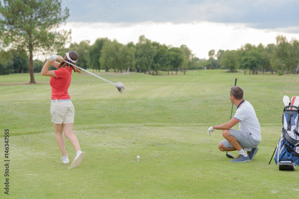 Obraz premium Woman playing golf, husband watching shot
