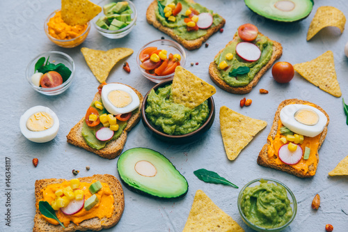 Guacamole and toasts. Fresh ingredients - avocado, tomatoes, onio, garlic, cilantro and crackers on gray background. Top view