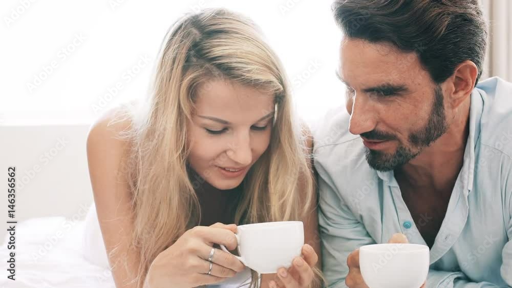 Couple talking while lying with a cup of coffee in their bedroom Couple talking while lying with a cup of coffee in their bedroom