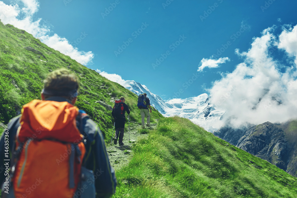 hikers with backpacks on the trail in the Apls, Swiss mountains. Trek near Matterhorn mount, mountain ridge on background