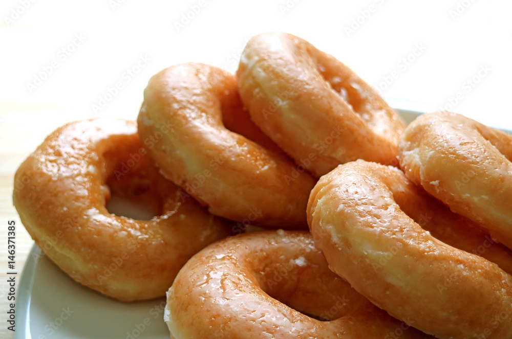 Piled up sugar-glazed doughnuts served on white plate, closed up, white background 