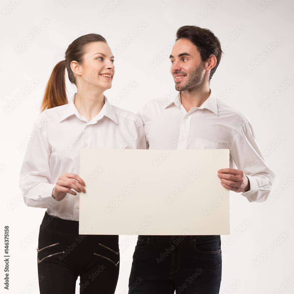 Young happy couple showing presentation pointing on placard over gray background Young happy couple showing presentation pointing on placard over gray background