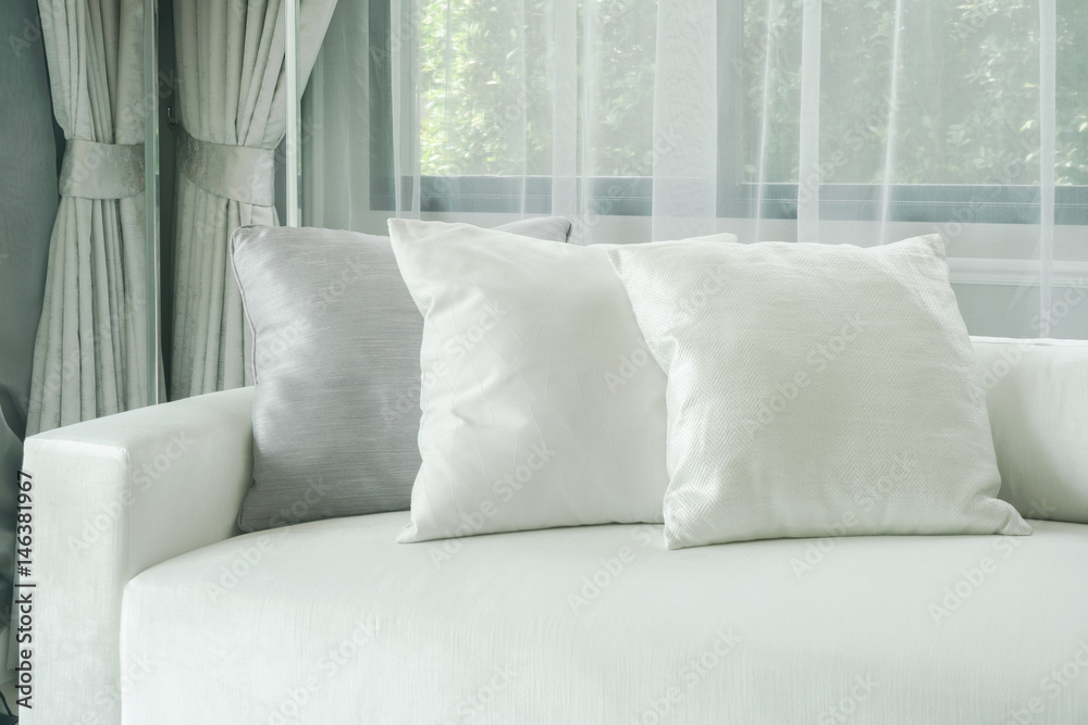 Fototapeta premium Pillows lay on white sofa with sheer curtain in background