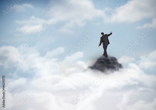 Business man losing balance on mountain peak in the clouds