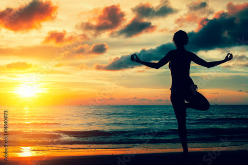 Woman practicing yoga on the ocean coast during a magical sunset. Silhouette. Exercise and meditation.