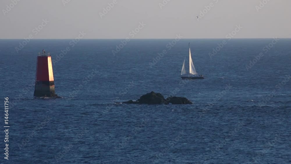 A sailboat passes a buoy near a rock in ocean, Brittany, France. A sailboat passes a buoy near a rock in ocean, Brittany, France.