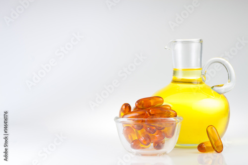 Fish oil in a jug and capsules over light grey background