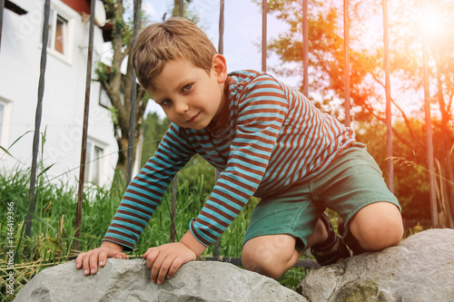 Small boy in striped sweater and shorts on big rocks in sunlight