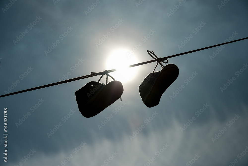 New-born child shoes hanging on the lace with clear sky and sun in background