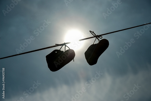 Obraz na płótnie New-born child shoes hanging on the lace with clear sky and sun in background w salonie