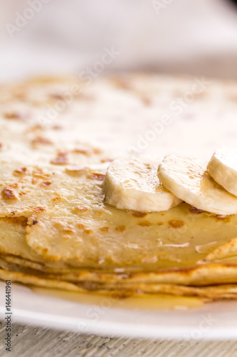 Thin pancakes with banana and honey. Maslenitsa. Russian pancakes on a light wooden background. In a rustic style.