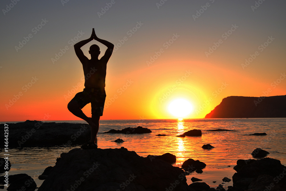 man practices yoga at sunset on the beach on a rock